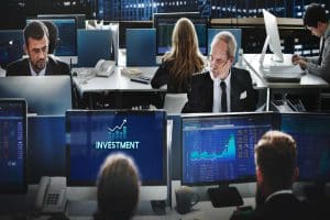 Investment professionals monitoring market trends and charts, analyzing real-time investment information on screens.