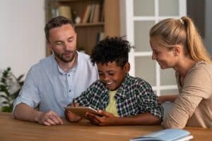 Smiling parents and child using a tablet together, sharing educational and digital information at home.
